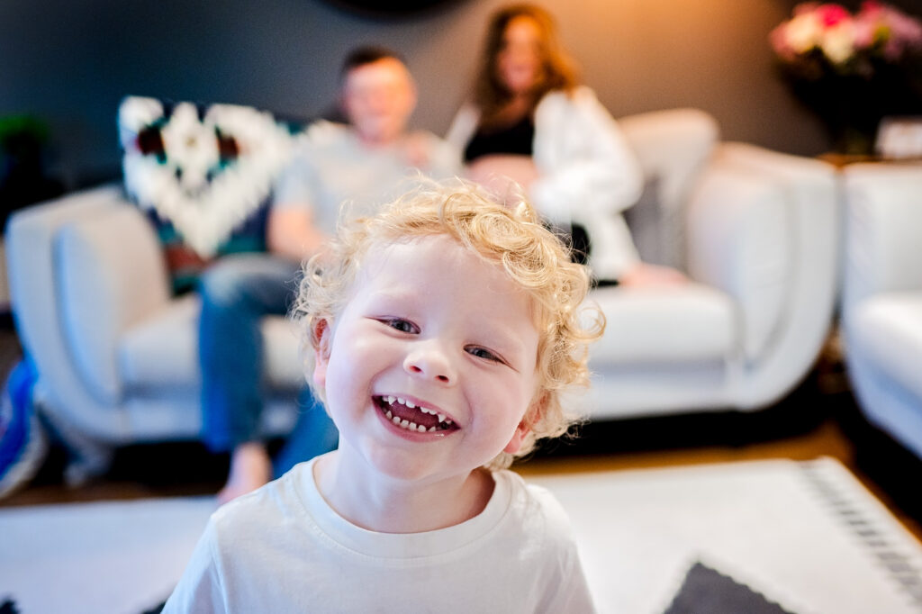 Happy boy smiling to the camera with his parents sitting behind him and looking at him proudly