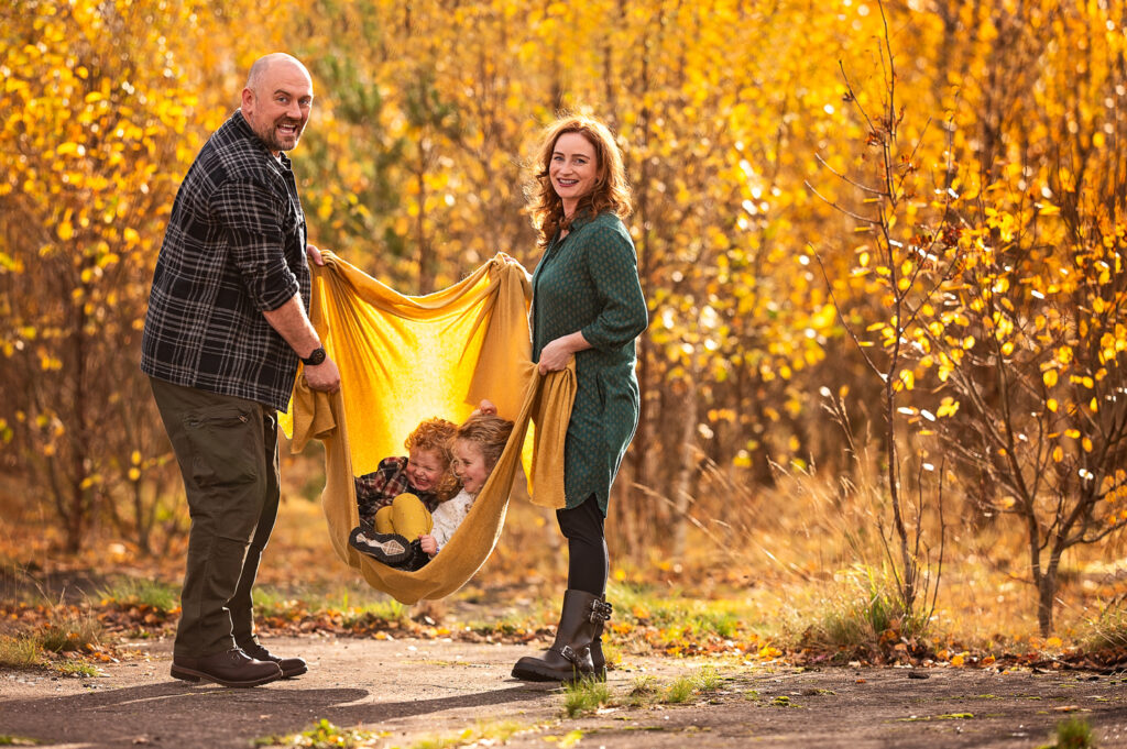 Parents playing with their children, they swinging them in the blanket during their family photoshoot on location in Glasgow.