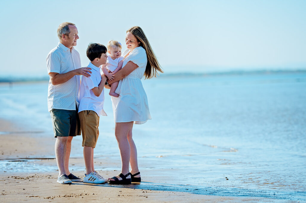 Family standing barefoot through shallow water during a sunny Irvine Beach family photoshoot in Scotland, captured by Ola Molik Photography