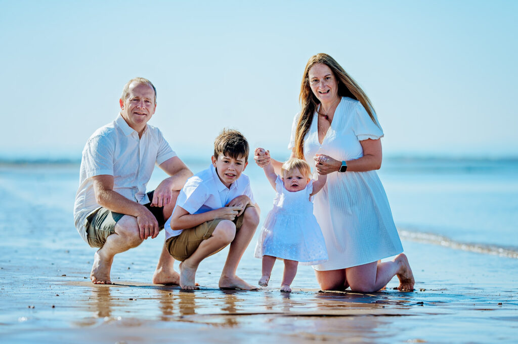 Family sitting barefoot on the shallow water during a sunny Irvine Beach family photoshoot in Scotland, captured by Ola Molik Photography