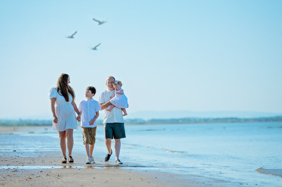 Family walking barefoot through shallow water during a sunny Irvine Beach family photoshoot in Scotland, captured by Ola Molik Photography