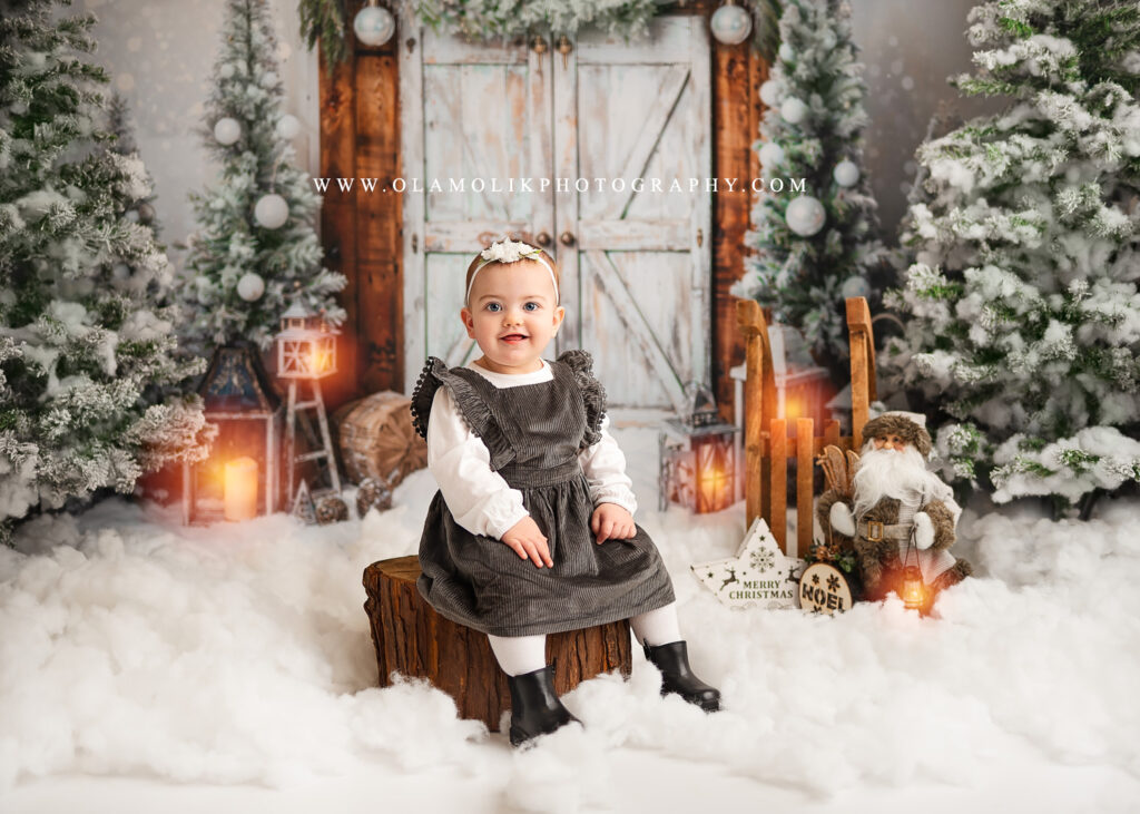 Baby Christmas photoshoot in Glasgow by Ola Molik Photography. A festive Bambino Christmas portrait featuring a baby on a snowy Christmas set with winter trees, lanterns and Christmas decorations. Christmas photography for babies and young children in Glasgow and Clydebank.