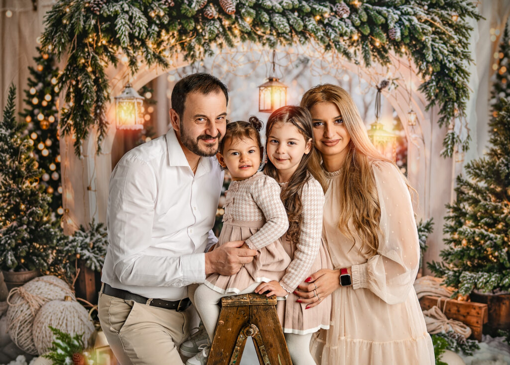 Family Christmas photoshoot in Glasgow by Ola Molik Photography, featuring parents and their two children on a warm winter Christmas set with festive greenery, Christmas trees and glowing lanterns. Christmas Mini Sessions available for families in Glasgow, Clydebank and surrounding areas.