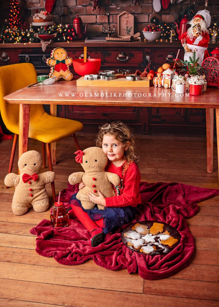 Girl sitting under the table cuddling a gingerbread soft toy during a Christmas photoshoot in Clydebank